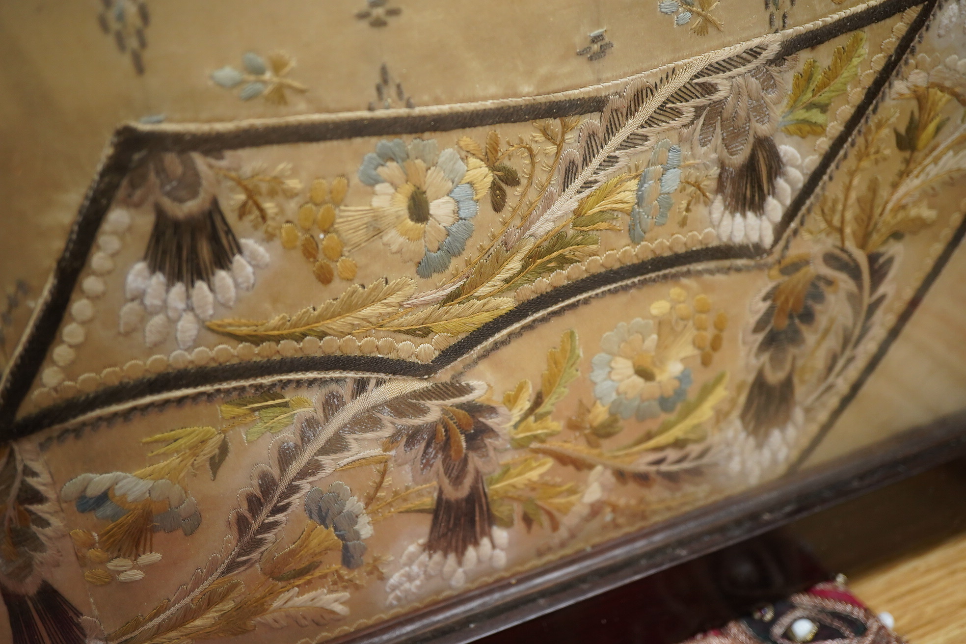 A framed front panel of a Regency silk embroidered waistcoat, ornately worked in fine polychrome silks with vining stems of leaves and hanging flowers framing a small spot motif interior, 60cm x 59cm. Condition - the sil